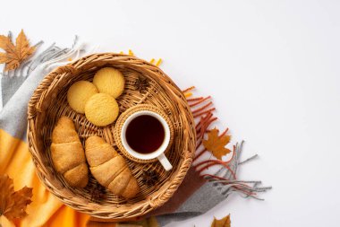 Autumn inspiration concept. Top view photo of wicker tray with cup of tea on rattan serving mat croissants cookies anise yellow maple leaves and plaid on isolated white background