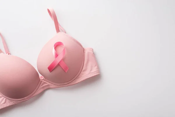 Top view photo of pink ribbon symbol of breast cancer awareness attached to pink bra on isolated white background with copyspace