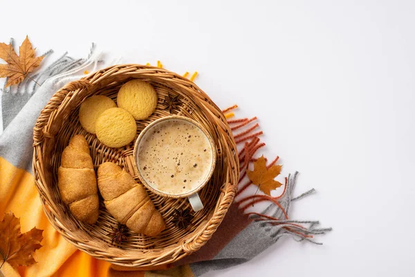 Autumn aesthetic concept. Top view photo of wicker tray with cup of frothy coffee croissants cookies anise yellow maple leaves and plaid on isolated white background