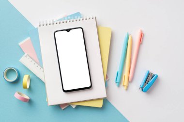 Back to school concept. Top view photo of school supplies smartphone over notebooks pens ruler stapler and adhesive tape on bicolor blue and white background with copyspace