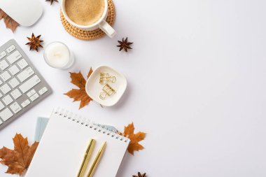 Autumn business concept. Top view photo of keyboard computer mouse notepad gold pen candle cup of coffee rattan serving mat binder clips yellow maple leaves and anise on isolated white background
