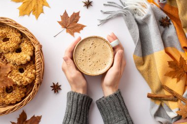 Autumn concept. First person top view photo of girl's hands in sweater holding cup of coffee wicker tray with cookies scarf fallen maple leaves anise and cinnamon sticks on isolated white background