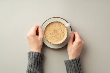 Autumn mood concept. First person top view photo of female hands in sweater holding saucer with mug of hot drinking on isolated grey background