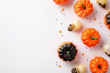 Halloween decorations concept. Top view photo of pumpkins skulls and confetti on isolated white background with copyspace