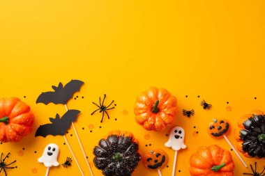 Halloween decorations concept. Top view photo of pumpkins ghost shaped lollipops spiders bat silhouettes and confetti on isolated orange background with copyspace