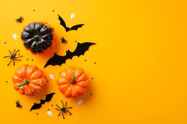 Halloween concept. Top view photo of pumpkins spiders ghost bat silhouettes and black confetti on isolated orange background with copyspace