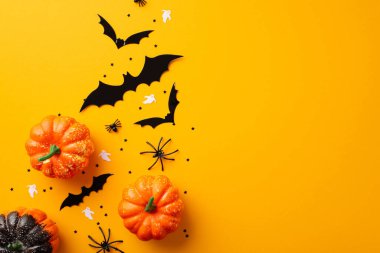 Halloween concept. Top view photo of pumpkins spiders ghost bat silhouettes and black confetti on isolated orange background with copyspace