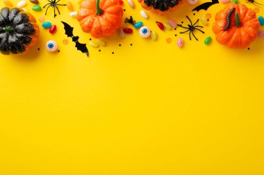 Halloween decorations concept. Top view photo of pumpkins spooky eyeballs centipede color candies spiders and confetti on isolated yellow background with empty space