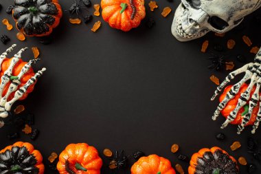 Halloween concept. Top view photo of pumpkins skull skeleton hands candies and spiders on isolated black background with empty space in the middle
