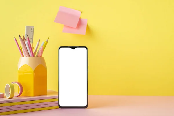 Back to school concept. Photo of smartphone stack of copybooks stand for pens adhesive tape and sticky note paper attached to yellow wall with copyspace
