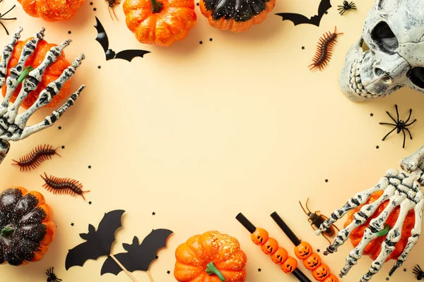 Halloween decor concept. Top view photo of pumpkins skeleton hands skull straws spiders cockroach centipedes and bats silhouettes on isolated beige background with empty space in the middle