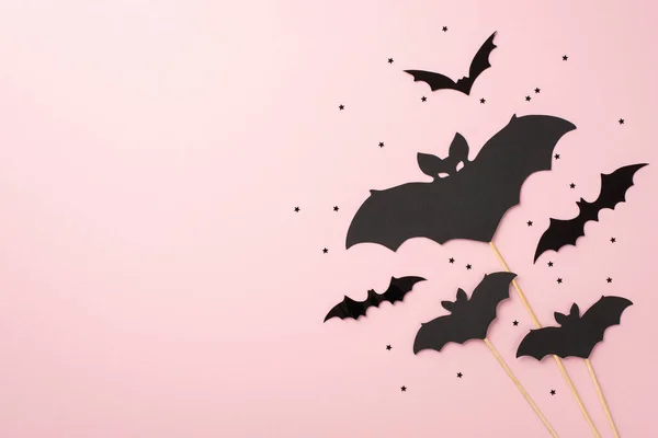 Halloween party decorations concept. Top view photo of bat silhouettes and black confetti on isolated pastel pink background with copyspace