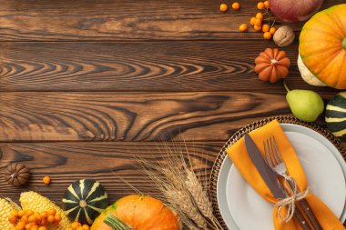 Thanksgiving day concept. Top view photo of plate knife fork napkin raw vegetables pumpkins apple pear maize walnut wheat and rowan on dark brown wooden desk background with copy space