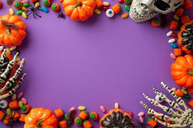 Halloween concept. Top view photo of pumpkins skull skeleton hands candies eyes spiders and centipedes on isolated violet background with copyspace in the middle