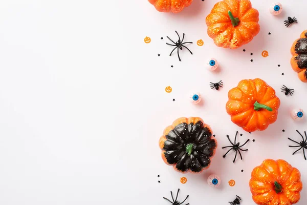 Halloween party decorations concept. Top view photo of pumpkins creepy eyes spiders and confetti on isolated white background with copyspace