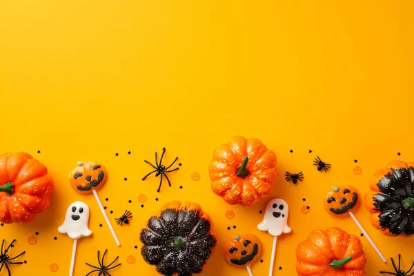 Halloween decorations concept. Top view photo of pumpkins ghost shaped lollipops spiders and confetti on isolated orange background with copyspace