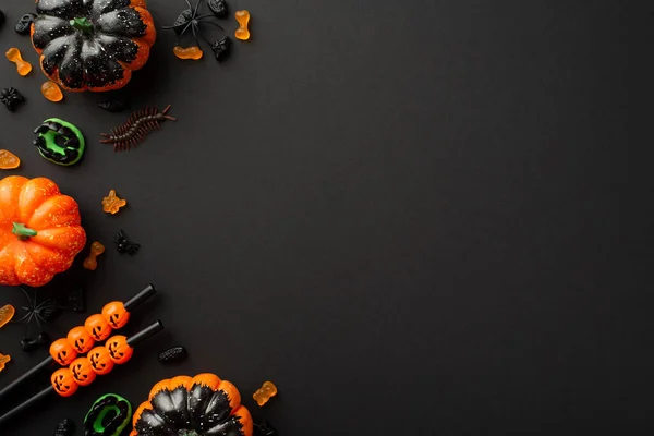 Halloween party decorations concept. Top view photo of pumpkins candies centipede cocktail straws and spiders on isolated black background with empty space