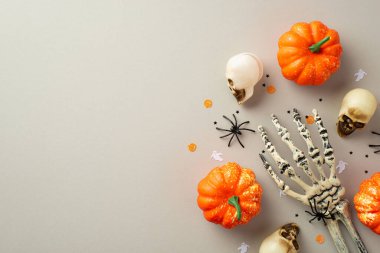 Halloween concept. Top view photo of skulls pumpkins spooky skeleton hand spiders and confetti on isolated grey background with copyspace
