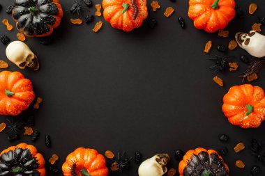Halloween creepy decorations concept. Top view photo of pumpkins skulls jelly candies centipedes and spiders on isolated black background with empty space in the middle