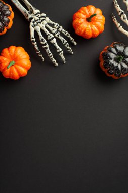 Top view photo of halloween decorations skeleton hands and pumpkins on isolated black background with empty space