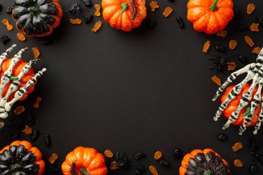 Halloween decor concept. Top view photo of skeleton hands holding pumpkins candies centipedes and spiders on isolated black background with copyspace in the middle