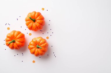 Halloween concept. Top view photo of orange pumpkins and confetti on isolated white background with copyspace