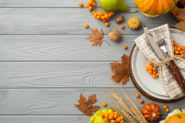 Thanksgiving day concept. Top view photo of plate knife fork napkin maple leaves raw vegetables pumpkins pear wheat walnut rowan and acorn on isolated grey wooden table background with copyspace