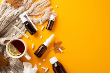 Disease concept. Top view photo of remedy bottles crumpled napkin pills capsules cup of tea with lemon thermometer maple leaves and knitted plaid on isolated orange background with copyspace