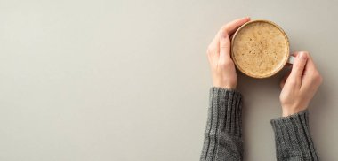 Autumn inspiration concept. First person top view photo of woman's hands in jumper holding mug of hot drinking on isolated grey background with empty space