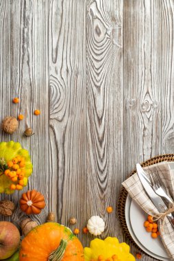 Şükran Günü konsepti. Tabak peçete bıçağının dikey fotoğrafı. Çiğ sebzeler, balkabakları, elmalı böğürtlenler, meşe palamutları, kopyalanmış gri ahşap masa arka planında.
