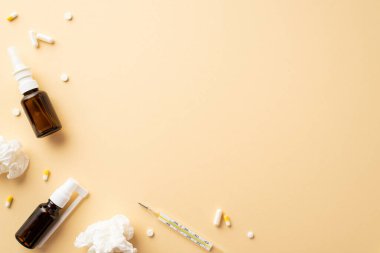 Hastalık konsepti. İlaç, burun ve boğaz spreyi, termometre ve buruşuk kağıt peçetelerin izole edilmiş bej arka plan ve boş alan.