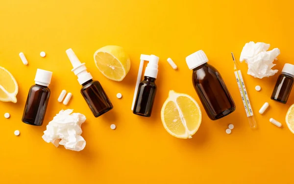 Disease concept. Top view photo of spray and syrup transparent brown bottles crumpled paper napkins pills capsules thermometer and lemon halves on isolated orange background