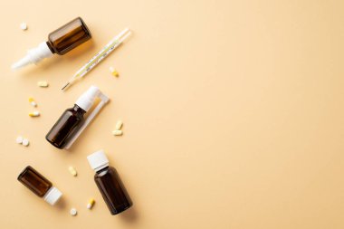 Hastalık konsepti. Tedavide kullanılan şeffaf kahverengi şişe hapları kapsülleri ve izole edilmiş bej arka planda termometre ve boş alan.