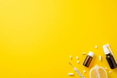 Hastalık konsepti. Tedavide kullanılan şeffaf kahverengi şişe hapları, termometre ve limon yarısını izole edilmiş sarı arka planda fotosu.