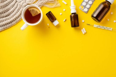 Hastalık konsepti. İlaç şurubu ve sprey şişeleri, su toplayan haplar, limon dilimli termometre çay ve kopyalanmış sarı arkaplan üzerine örülmüş eşarp.