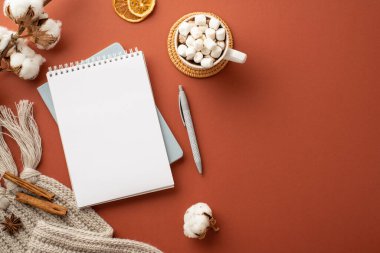 Açık günlüklü ekoseli kakao fotografının üst görüntüsü. Üzerinde marshmallow ve rattan yapılmış portakal dilimleri. Tarçın, izole edilmiş kahverengi arka planda pamuk dalları.