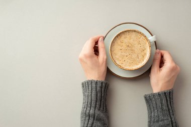 Sonbahar konsepti. Örgü kazaklı, elinde bir fincan sıcak köpüklü çay tabağıyla genç bir kadının ellerinin, izole edilmiş gri arka planda, kopyalanmış bir şekilde içki içerken çekilmiş ilk resmi.