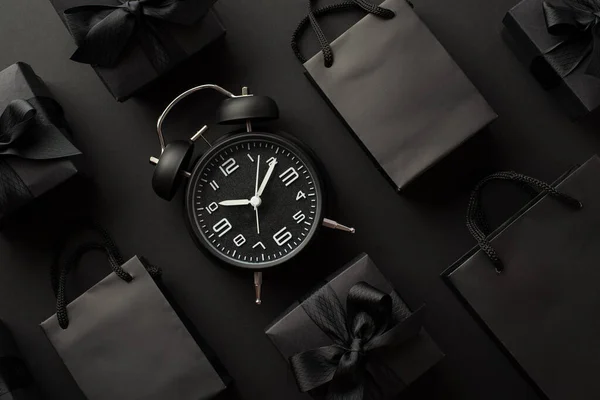 黑色星期五销售概念 黑色警钟礼品盒的顶部照片 礼品盒上有彩带蝴蝶结和黑色背景的时髦纸袋 — 图库照片
