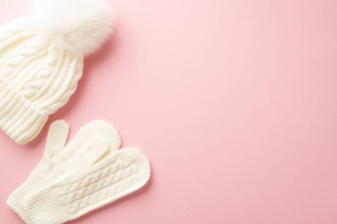 Kış mevsimi konsepti. İzole edilmiş pastel pembe arkaplandaki beyaz boncuk şapkalı ve örülmüş eldivenlerin fotosu.