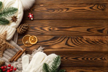 Noel dekorasyonu konsepti. Şapka fotoğrafı ekose eldivenler ladin dalları hasır yıldız kurutulmuş portakal dilimleri ökse otu üzümleri ve tarçın çubukları ahşap masa arkasında kopyalanmış.