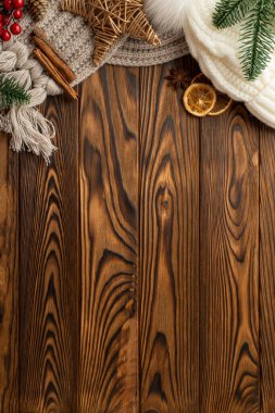 Noel konsepti. Hasır yıldız ökseotu üzümlerinin dikey fotoğrafı. Şapka örülmüş eşarp çam dalları tarçın çubukları kurutulmuş portakal dilimleri ve ahşap masa arkasında boş alan.