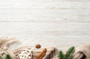 Kış estetiği konsepti. Çam ağacından dalların üst görüntüsü bir fincan kakao marshmallow kaplı örgü eşarp anason ve tarçın çubukları beyaz ahşap masa arka planında boş alan