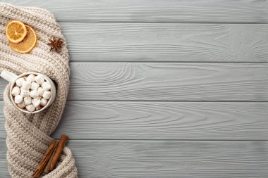 Kış estetiği konsepti. Marshmallow örülmüş portakal dilimleri anason ve tarçın çubuklarıyla dolu bir bardak sıcak içkinin fotosu. Gri ahşap masa arka planında.