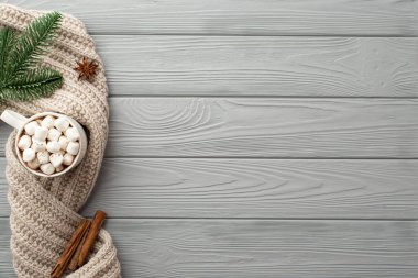 Kış estetiği konsepti. Marshmallow örgü eşarp çam dalı anason ve tarçın çubuklarıyla dolu bir fincan sıcak içkinin resmi. Gri ahşap masa zemininde.