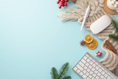 İş yerindeki klavye bilgisayar faresi fincanının üst görüntüsü kalem örgü çam dalları ökseotu dilimleri ve izole edilmiş pastel mavi arka planda tarçın çubukları.