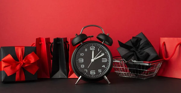 黑色星期五销售概念 黑色桌上型红墙背景购物车上的闹钟红色和黑色纸袋和带蝴蝶结礼品盒的照片 — 图库照片