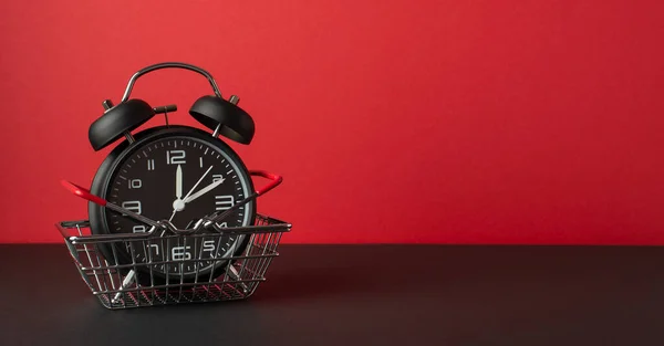 ブラックフライデーのコンセプト 黒いテーブルの上のショッピングカートの黒い目覚まし時計の写真空のスペースと赤い壁の背景 — ストック写真
