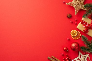 Noel arifesi kavramı. Süslemelerin üst görüntüsü köknar dalları kağıt hediye kutusu hasır yıldızı kurutulmuş portakal dilimleri izole edilmiş kırmızı zemin üzerinde ökse otu tarçın.