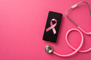 Göğüs kanseri farkındalığı konsepti. Stetoskop ve pembe ipek kurdelenin izole edilmiş pembe arka planda akıllı telefon üzerinden en üstteki görüntüsü.
