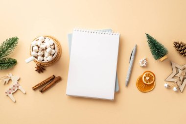 Kış tatili konsepti. Açık not defterinin üst görüntüsü kalem ahşap süslemeleri köknar dalı kozalaklı kakao fincanı marshmallow kurutulmuş portakal dilimleriyle izole edilmiş bej arka planda tarçın ve kopyasal alan